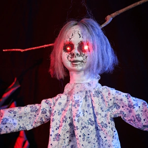 Scary Halloween hanging doll with glowing red eyes and floral dress on tree branch