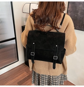 Retro black matte backpack with silver buckles worn by model in a stylish cozy outfit