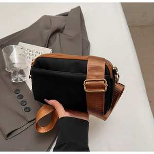 Detailed view of a black crossbody bag with brown strap and gold metal buckle adjusters
