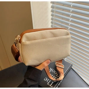 Detail view of beige canvas crossbody bag with brown trim and gold metal hardware