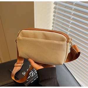 Detail of a beige canvas mini crossbody bag with brown nylon strap and gold hardware