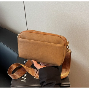 Detail of a brown fabric crossbody bag featuring double zippers and a wide nylon strap