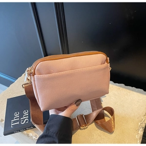 Detail of pink fabric crossbody bag featuring wide brown nylon strap and gold-tone zippers