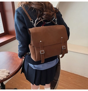 Brown matte retro backpack with flap and buckle details worn by model in a vintage setting
