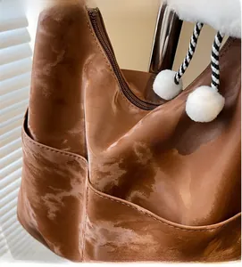 Close-up of brown shoulder bag with cloud texture, metal zipper and plush pom-pom charm