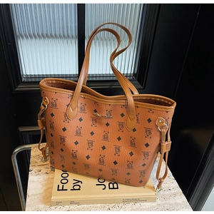 Detail of brown tote bag featuring teddy bear print and golden metal logo plaque