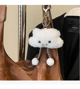 Close-up of white plush cloud charm with striped legs hanging on a brown leather tote bag