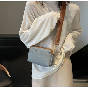 Detail of grey crossbody square bag featuring dual zippers and brown woven shoulder strap