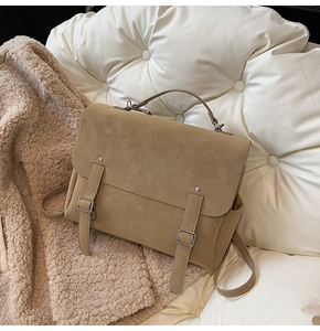 Detail of vintage matte brown satchel bag with buckle straps and top handle on soft background