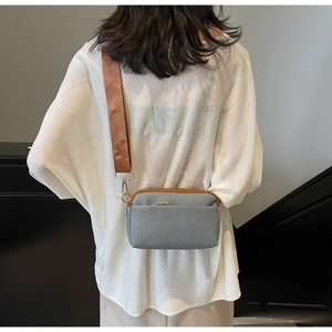 Detail of light blue crossbody bag with brown nylon strap and gold-tone zipper closure