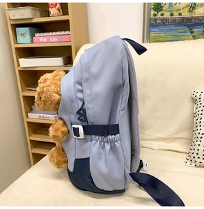 Detail of blue nylon backpack with side buckle and a cute brown teddy bear accessory