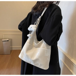 Detail of white wrinkled hobo bag with plush bear charm and front pocket shown on model