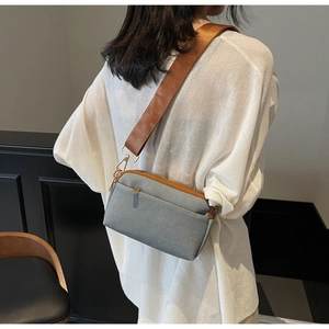 Detail of grey canvas crossbody bag with brown straps worn by a model in a casual setting