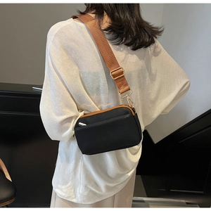 Detail of a black leather crossbody bag with a trendy wide brown woven strap on a model