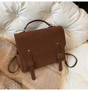 Detailed close-up of brown matte texture bag with twin buckle straps and top handle