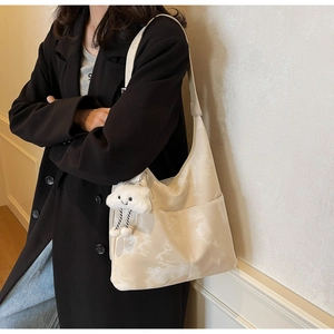 Detail view of beige shoulder bag with cloud patterns and plush cloud pendant charm