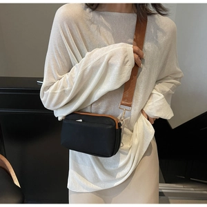 Close-up of black minimalist crossbody bag featuring dual zippers and woven brown strap