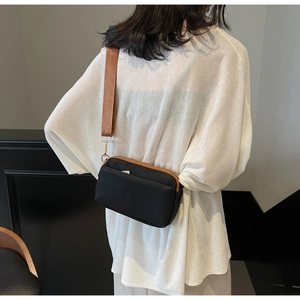 Detail of minimalist black nylon crossbody bag with brown woven strap and gold zippers