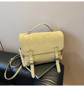 Detail of a yellow vintage satchel bag with metallic buckles on a black leather sofa