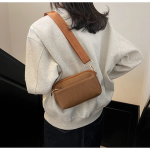 Close-up of brown canvas crossbody bag with wide nylon strap and gold hardware detail