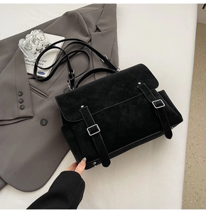 Detailed close-up of a matte black messenger bag with dual buckle straps on a grey blazer