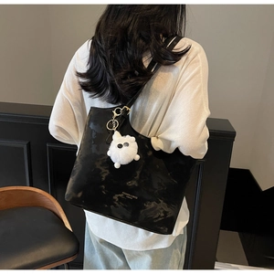 Detail of black marble textured tote bag with a cute white fuzzy charm on a shoulder strap