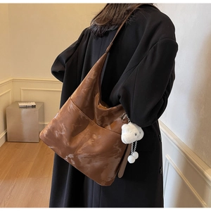 Detail of large brown leather tote bag with marble texture and white pompom charm on model