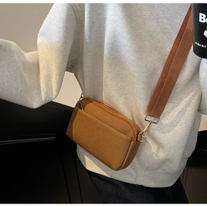 Detail of caramel brown canvas crossbody bag featuring double zippers and wide nylon strap