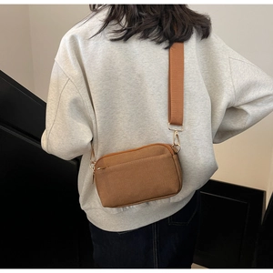 Rear view of model wearing a brown canvas crossbody bag with wide strap and gold hardware