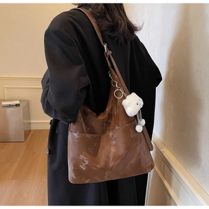 Detail of a brown leather tote bag with a plush bear charm worn by a model