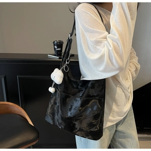 Detail of glossy black tote bag with textured finish and cute plush charm on shoulder
