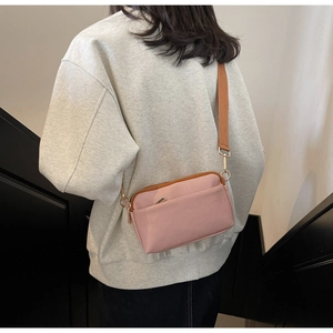 Pink minimalist crossbody bag with wide brown strap and front zipper pocket detail
