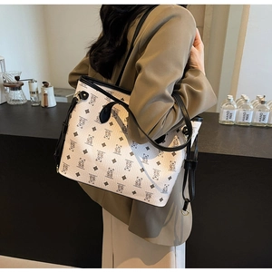 Detail of cream tote bag with bear pattern and black straps on model in olive suit