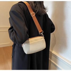 Detail of a minimalist cream canvas crossbody bag with a wide brown textile strap on a model
