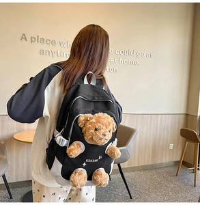 Close-up of the black canvas backpack with a 3D plush teddy bear charm and strap detail