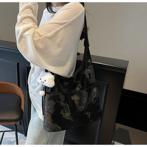 Detail of black tote bag with glossy texture and a cute white plush bear pendant accessory