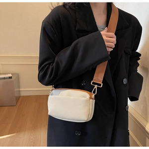Detail of a cream canvas crossbody bag with a wide brown strap worn by a model