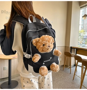 Close-up of black and white canvas backpack with a 3D plush bear and side buckles