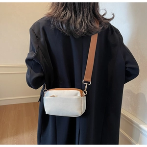 Detail of off-white crossbody bag featuring a wide brown fabric strap and golden hardware