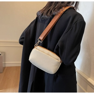 Detail of cream fabric crossbody bag with gold hardware and wide tan strap on black blazer