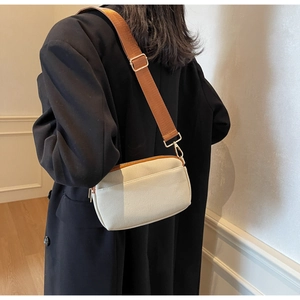 Detail view of a cream canvas crossbody bag with broad brown strap on a model wearing black