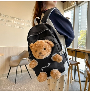 Detail shot of a black nylon backpack featuring a cute 3D brown plush teddy bear insert