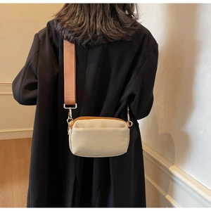 Close-up of cream square crossbody bag with brown nylon strap on black coat background