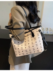 Chic beige tote bag with bear monogram pattern and black leather handles shown by a model