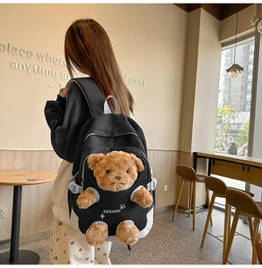 Close-up of black backpack with a 3D plush teddy bear detail and white logo