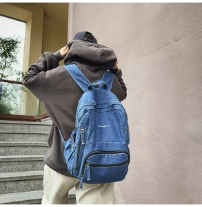 Detalle de mochila vaquera azul oscuro con bordado blanco y correas anchas denim