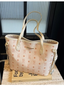 Chic beige tote bag with bear pattern and gold logo plaque on a cookbook background