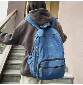 Vista trasera de una mochila de mezclilla lavada azul con bolsillos de cremallera en modelo