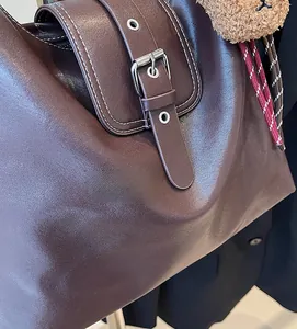 Detail der dunkelbraunen Leder-Tote-Bag mit Kontrastnähten und Plüschbär-Anhänger