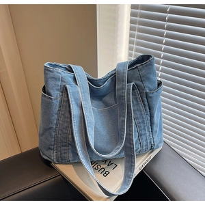 Gros plan sur la texture du denim bleu délavé et la poche latérale du grand sac cabas